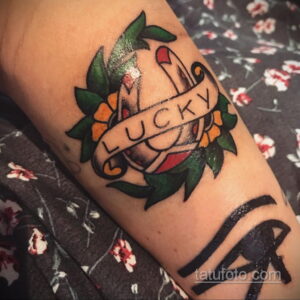 Фото тату подковы с надписью "LUCKY" на предплечье. Рисунок татуировки в стиле олд скул с использованием красного, черного и желтого цветов.