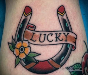 Фото тату подковы с надписью "LUCKY". Яркий рисунок татуировки в стиле олд скул с использованием красных, желтых и черных цветов.