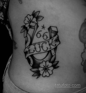 Фото тату подковы с надписью 'LUCK' и цветами в черно-белом стиле на боку. Рисунок татуировки с детальной проработкой контуров и теней.