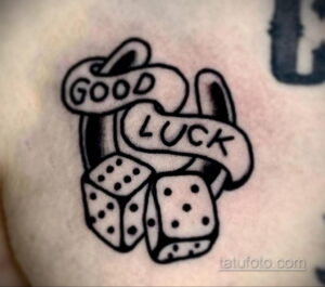 Черно-белое фото тату на коже с изображением игральных костей и надписи 'GOOD LUCK' на ленте. Простой, но символичный рисунок.