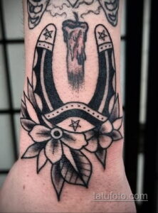 Фото тату подковы, свечи и звезд в стиле blackwork на руке. Черно-белая татуировка, детализированная проработка теней и узоров.