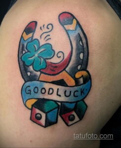Фото тату на плече: подкова, клевер, кубики и надпись 'Good Luck' в стиле олд скул. Яркие цвета, четкие контуры, классический дизайн.