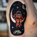 Фото тату на руке: космонавт, луна, Земля, звезды, яркие цвета. Красочный и детализированный рисунок татуировки.
