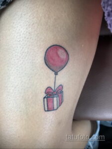 Фото тату воздушного шарика с подарком в акварельном стиле на руке. Нежные цвета, легкие мазки, милый и трогательный дизайн. Идеально для девушек, любящих романтику.