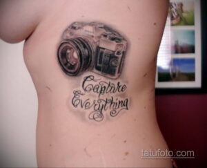Фото тату камеры и фразы 'Capture Everything' на боку. Черно-белый рисунок в реалистичном стиле.