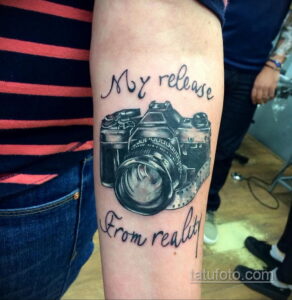 Фото тату винтажного фотоаппарата с надписью 'My release from reality' на руке, выполненное в стиле графика с использованием черных чернил.