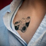 Фото тату контурного фотоаппарата на груди мужчины. Простой и элегантный рисунок татуировки в стиле лайнарт.
