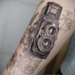 Детализированная татуировка старинной камеры Ikoflex с надписью Zeiss Ikon на руке. Реалистичный рисунок татуировки для ценителей винтажной техники.