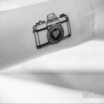 Фото тату минималистичного фотоаппарата на руке. Черно-белый рисунок, сердце вместо объектива, простой дизайн.