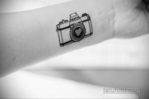 Фото тату минималистичного фотоаппарата на руке. Черно-белый рисунок, сердце вместо объектива, простой дизайн.