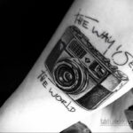 Фото тату черно-белого фотоаппарата на руке с надписью 'The way I see the world'. Реалистичный рисунок, каллиграфический шрифт.