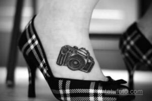 Фото тату: небольшой черно-белый рисунок фотоаппарата на лодыжке девушки. Изящная и минималистичная татуировка.