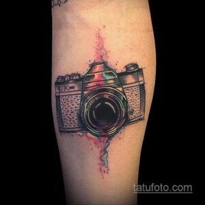 Фото тату винтажной камеры Nikon, выполненной в акварельной технике с брызгами краски. Яркий и красочный рисунок татуировки.