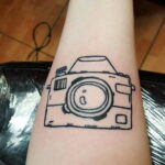 Фото тату винтажного фотоаппарата на предплечье. Детализированный рисунок татуировки в черно-белом стиле.