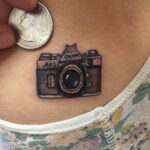 Фотография небольшой татуировки фотоаппарата на груди. Милый и аккуратный рисунок в ярких цветах.