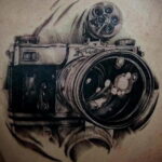 Фотография мужской татуировки фотоаппарата с добавлением эффекта дыма и шестеренок. Черно-белый рисунок с высокой детализацией.