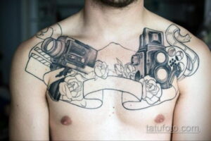 Фото тату: большая татуировка на груди с изображением фотоаппаратов, цветов и ленты. Черно-белый рисунок, детализированный дизайн, сложная композиция.