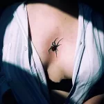 Фото тату: маленькая, минималистичная татуировка паука, выполненная в черном цвете под грудью. Изящный и деликатный рисунок.