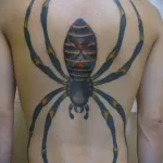 Фото тату большого паука на спине. Детализированный рисунок татуировки, выполненный в реалистичном стиле, с использованием ярких цветов.