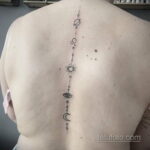 Фото татуировки на спине с изображением планет, символов, глаза и других космических элементов. Черно-белый рисунок в минималистичном стиле.