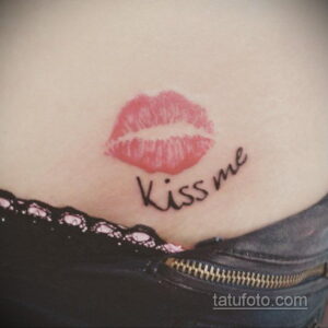 Фото тату на животе: красные женские губы и надпись 'Kiss me' выполнены в простом и романтичном стиле. Подчеркивает женственность и страсть.