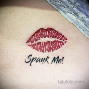 Фото тату с надписью "Spank Me!" и изображением красных губ на животе. Татуировка выполнена в минималистичном стиле и имеет провокационный характер.