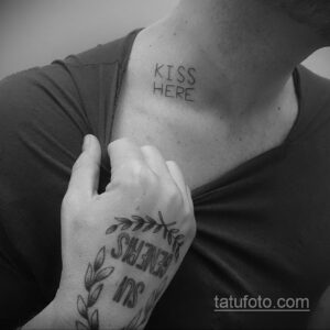 Фото тату с надписью "KISS HERE" на ключице и небольшим цветком на руке. Черно-белый минималистичный рисунок татуировки.