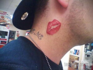 Фото тату: красные губы на шее мужчины и надпись 'Kiss Me' под ними. Простой и выразительный дизайн татуировки.