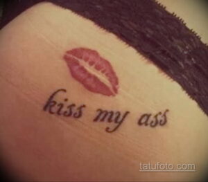 Фото тату на коже: отпечаток губ в розовых тонах с надписью 'kiss my ass'. Смелый и дерзкий эскиз татуировки, выражающий протест и независимость.