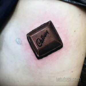 Фото тату с изображением плитки шоколада Cadbury на руке. Минималистичный рисунок татуировки с реалистичной проработкой деталей.