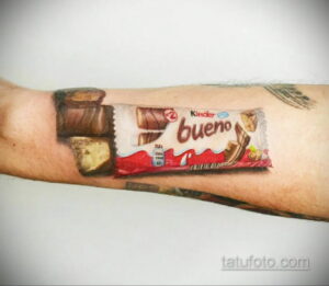 Фото тату на руке с гиперреалистичным изображением шоколадного батончика Kinder Bueno. Рисунок выполнен в ярких цветах с использованием техник реализма и акварели.