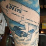 Фото тату: большая реалистичная татуировка самолета Delta на руке, с детальной проработкой и использованием синих и белых оттенков.