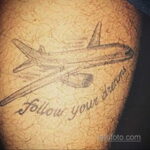 Фотография татуировки самолета на плече с надписью "Follow your dreams". Реалистичный рисунок, выполненный в черно-серых тонах.