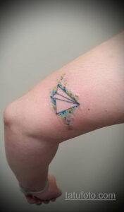 Фото тату: яркий акварельный рисунок бумажного самолетика с брызгами краски на локте.