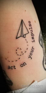 Фото тату на руке: бумажный самолетик и надпись "Act on your impulse". Минималистичный рисунок татуировки с вдохновляющим посланием.