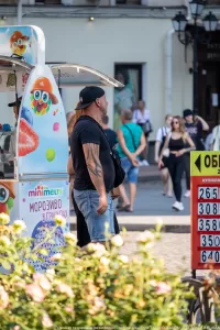 Фото тату на руке мужчины, идущего по улице с женщиной. Татуировка выполнена в темных тонах и покрывает большую часть предплечья.