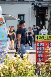 Фото тату на руке мужчины, идущего по улице с женщиной. Татуировка выполнена в темных тонах и покрывает большую часть предплечья.