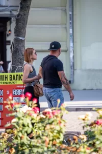 Фото тату на руке мужчины, идущего по улице с женщиной. Татуировка выполнена в темных тонах и покрывает большую часть предплечья.