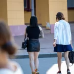 Фото тату на ноге и руке у девушки, идущей по улице. Вид сзади, татуировки в ярких цветах, современный стиль.
