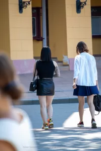 Фото тату на ноге и руке у девушки, идущей по улице. Вид сзади, татуировки в ярких цветах, современный стиль.