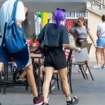 Фото девушки с татуировками на руках и ноге, идущей по улице. Видны тату в стиле олдскул на предплечье и лодыжке.