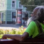 Фото татуировки на шее мужчины с длинной седой бородой. Рисунок выполнен в черном цвете, детализированный и символичный.