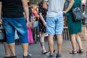 Фото тату на ноге девушки: небольшой рисунок, расположенный на икре. Девушка в летней одежде стоит в окружении людей на городской улице.