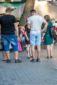 Фото тату на ноге мужчины: небольшой рисунок, расположенный на икре. Мужчина стоит в окружении людей на городской улице.