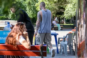 Фото мужчины с татуировками на руках и шее, сидящего за столиком в кафе с девушкой. Видны детализированные рисунки.