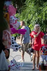 Фото тату на руках и шее мужчины, стоящего на улице. Видны татуировки в черном цвете. Мужчина держит воздушные шары.