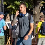 Фотография мужчины с татуировкой на руке, идущего по улице и разговаривающего по телефону. Татуировка выполнена в темных тонах и имеет сложный узор.