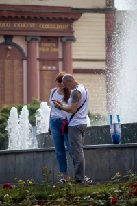 Фото татуировки дракона на руке женщины. Рисунок выполнен в черном цвете и имеет детализированную прорисовку. Женщина стоит возле фонтана.