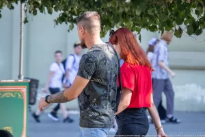 Фотография мужчины с татуировкой на предплечье, идущего с девушкой по улице. Татуировка выполнена в черных тонах и изображает растительный орнамент.