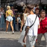 Фотография мужчины с татуировками на руках, идущего по улице в окружении других людей. На заднем плане видны здания и вывески.